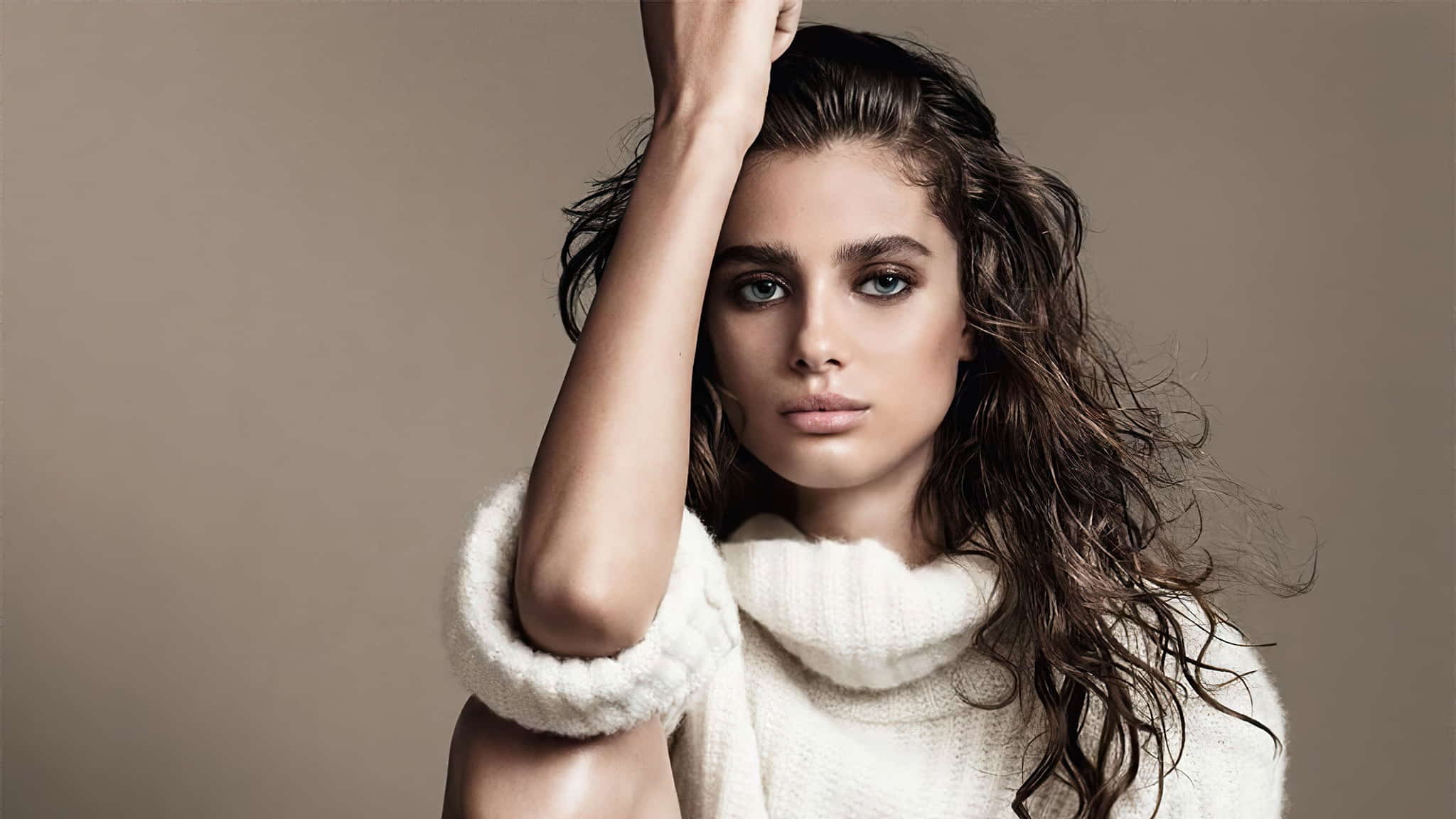 Taylor wearing a white sweater dress, posing in front of a light brown background