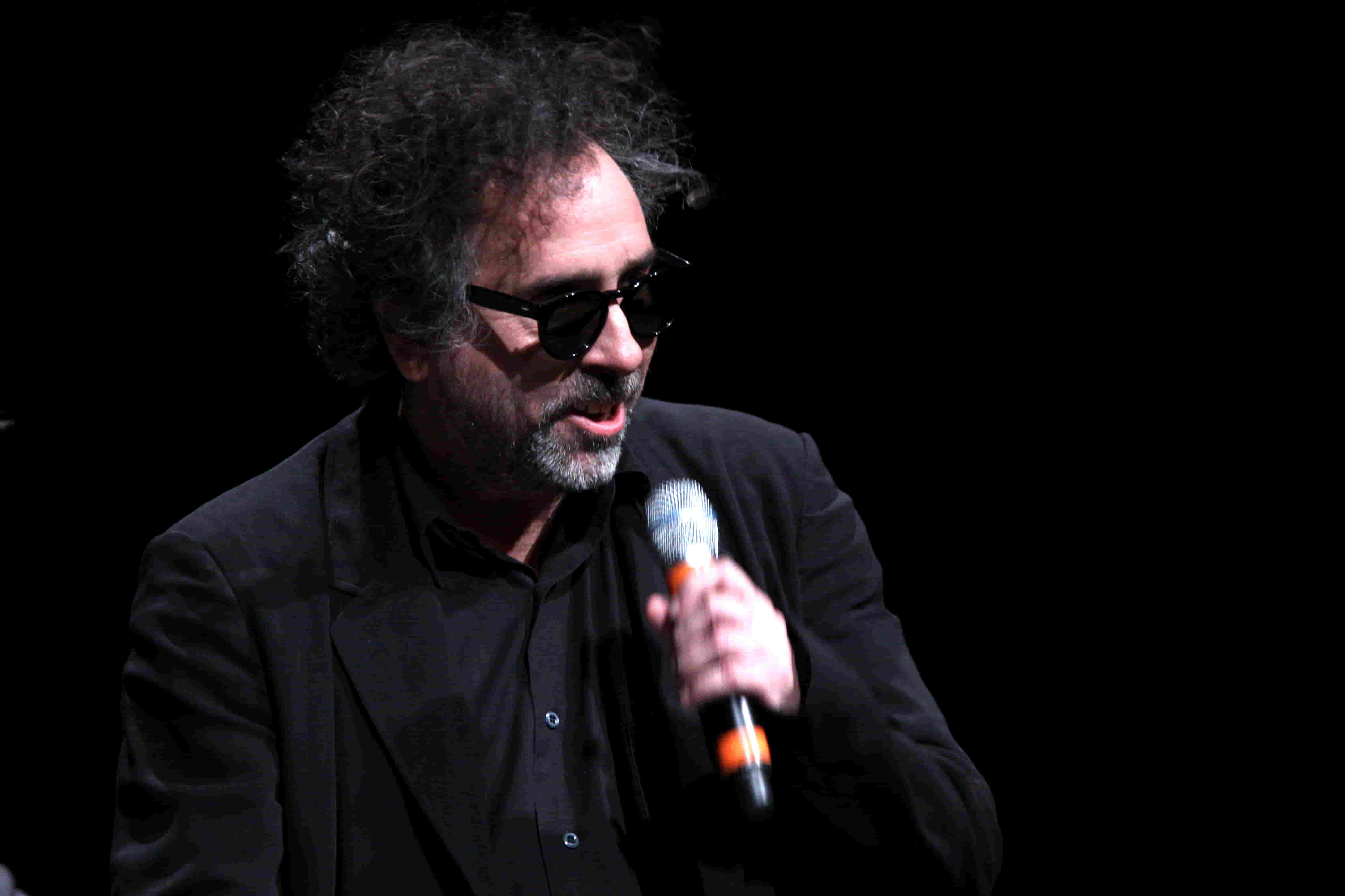 Tim Burton on a stage holding a microphone and addressing the audience