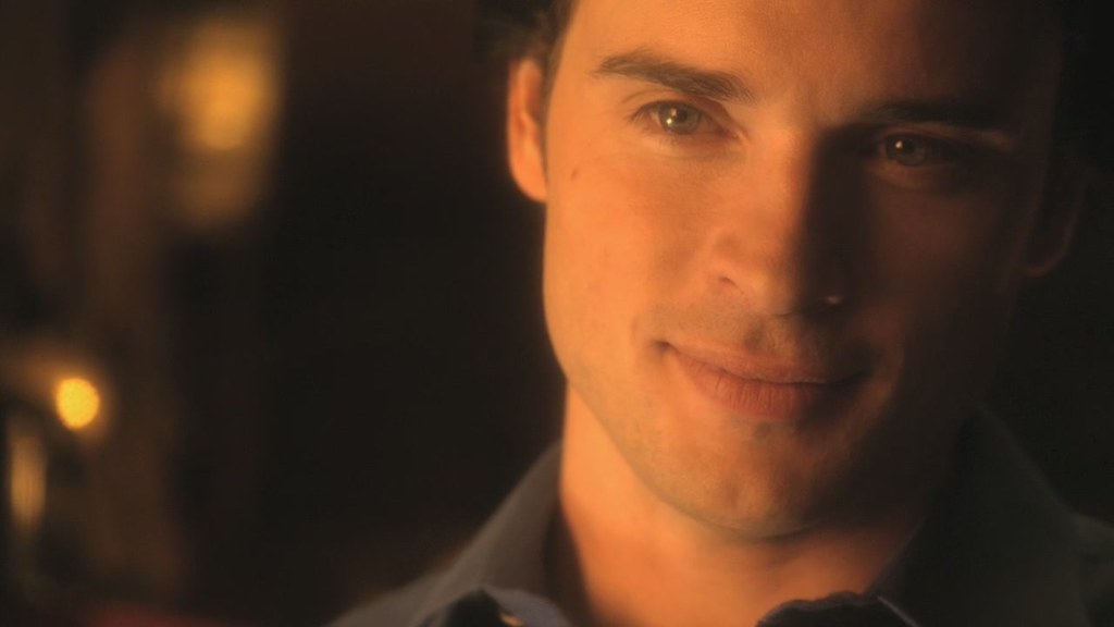 Close up image of Tom Welling, smiling in a dark colored shirt.