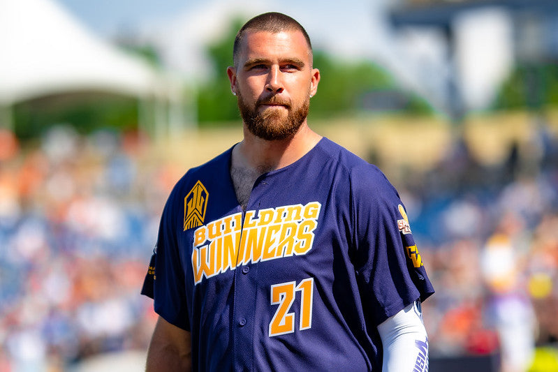 Travis Kelce in a blue jersey, standing in a playground with the audience in the background.