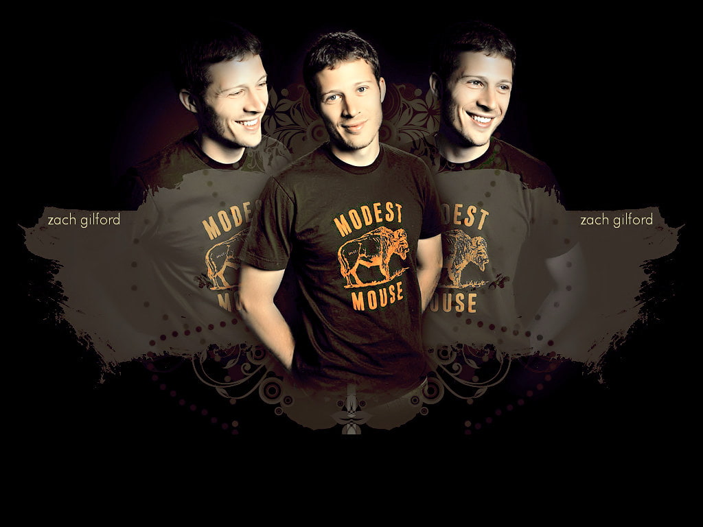 Zach Gilford wearing a black T-shirt with a logo of a buffalo and the words Modest Mouse on it. There are three figures of him looking in different directions.