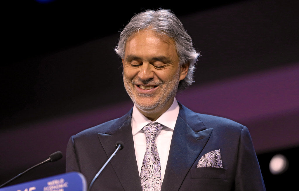 Andrea Bocelli formally dressed, addressing people at a conference. 