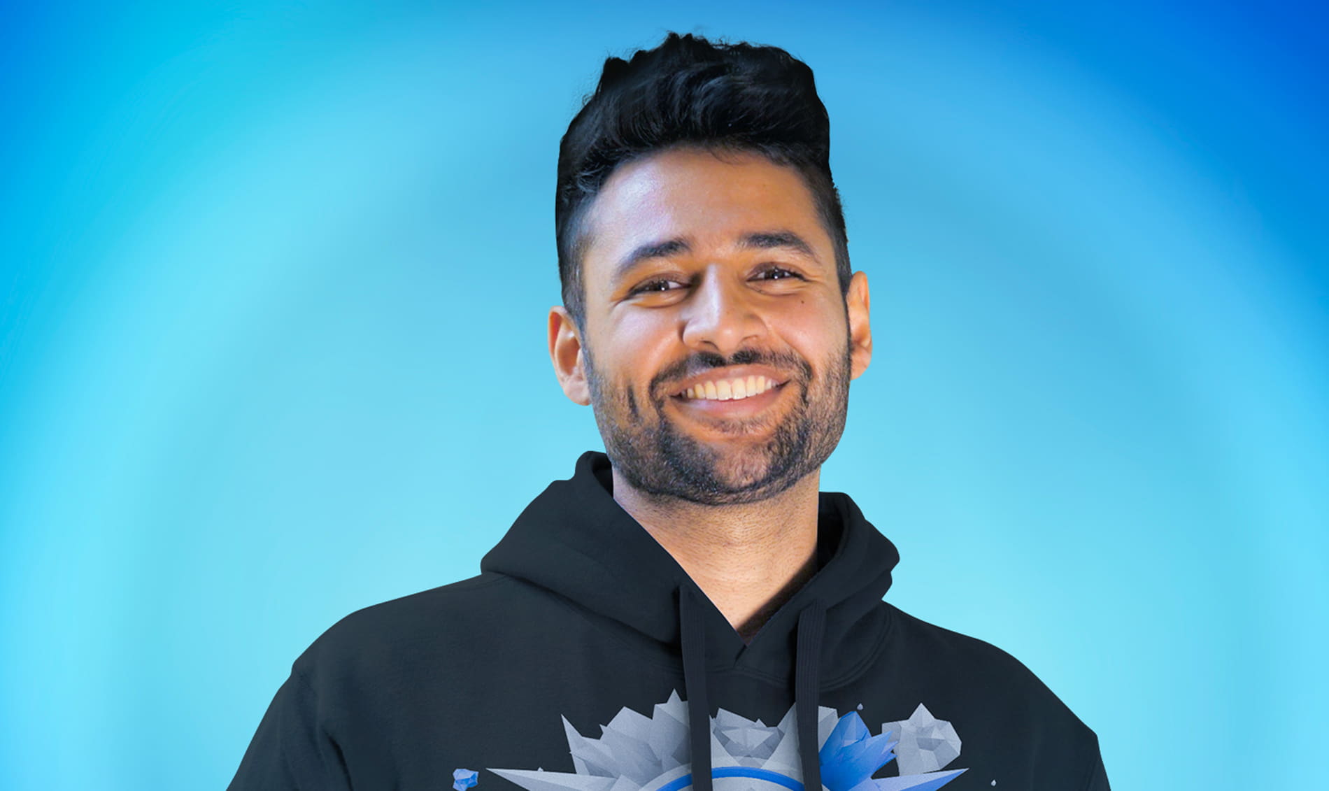 Arun Maini in a black hoodie, smiling while posing in front of a blue background.