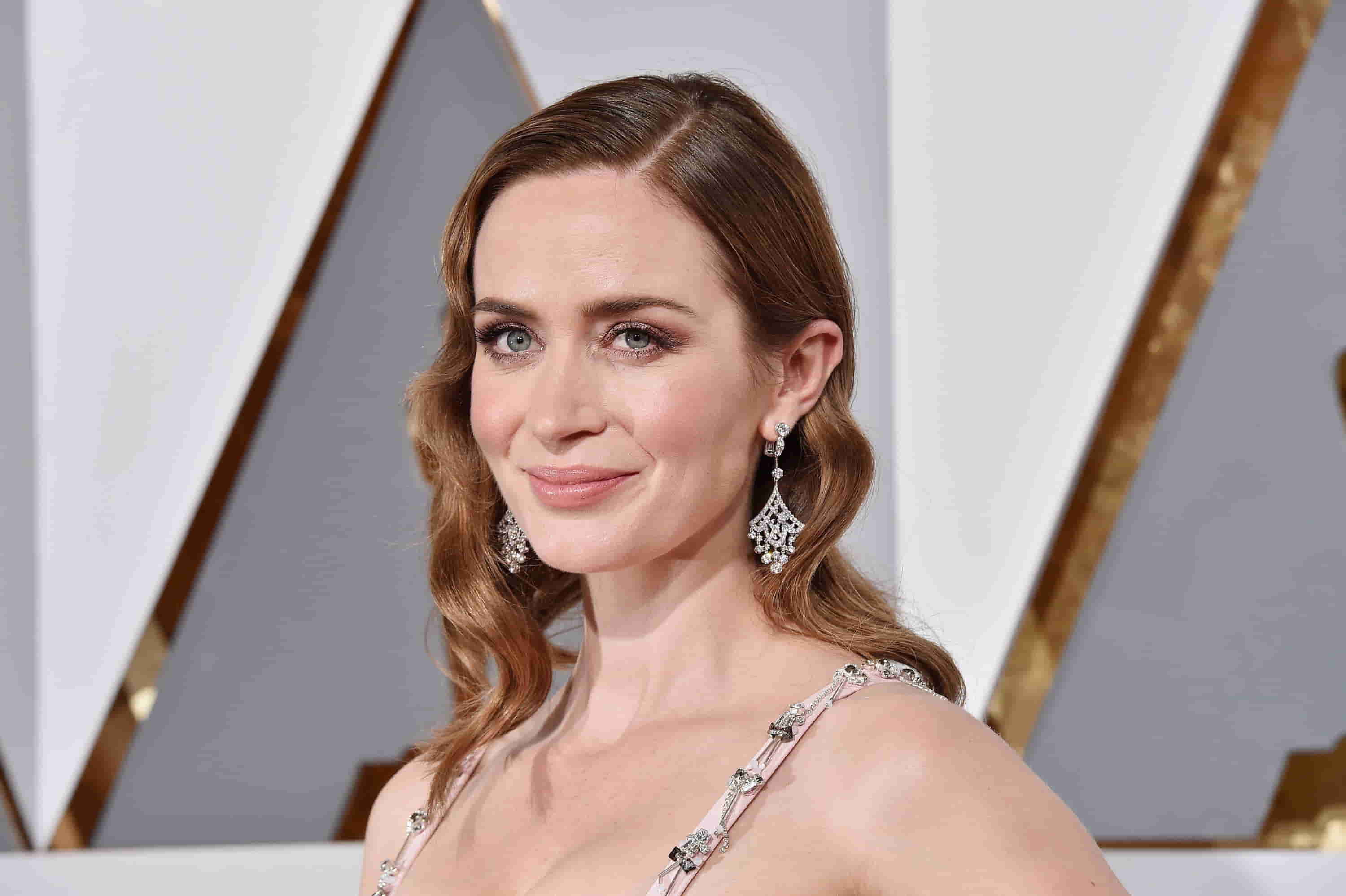 Emily Blunt at an awards ceremony, dazzling in a shimmering gown and elegant diamond earrings, posing gracefully for the cameras.