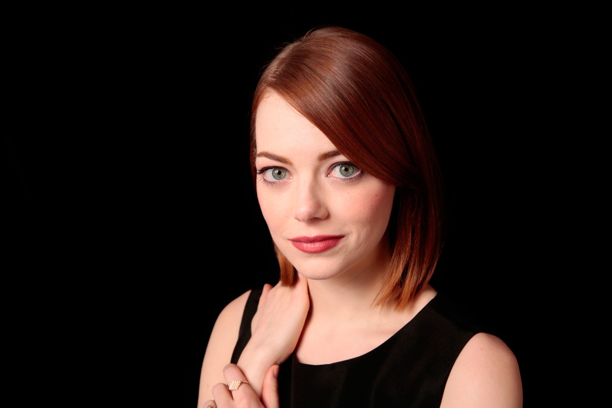 Emma in pitch black background, posing with right hand on her shoulder