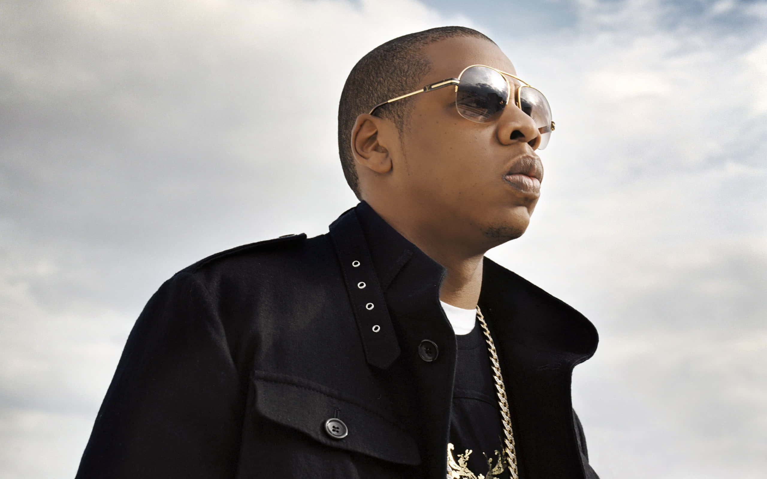 Jay-Z wearing black colored shades and jacket, posing with sky in the background.