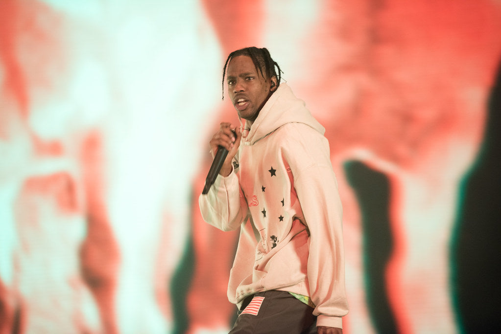 Travis Scott, in a white sweatshirt, holding a mic in his hand and performing at his concert